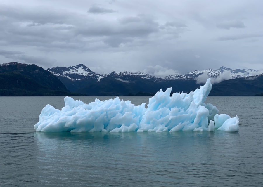 Melted portion of an iceberg floating in the middle of the Arctic with mountains in the background.
